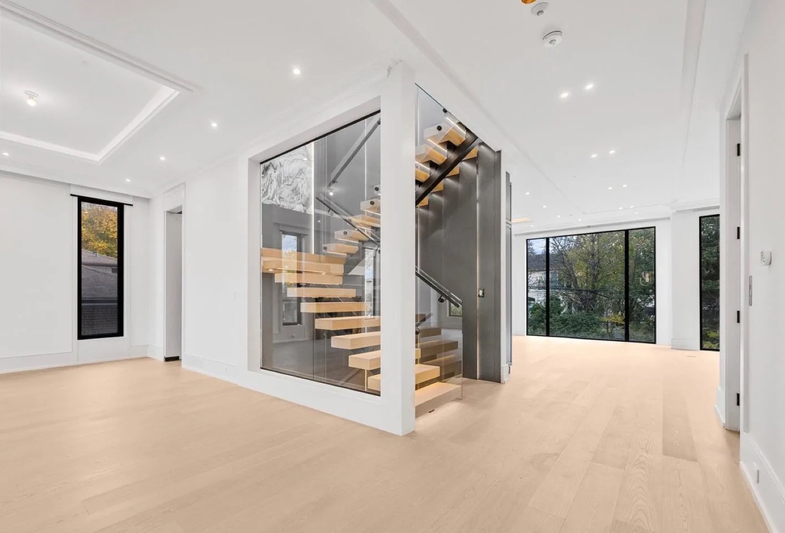 Open-riser oak staircase with a glass enclosure and wide plank floors